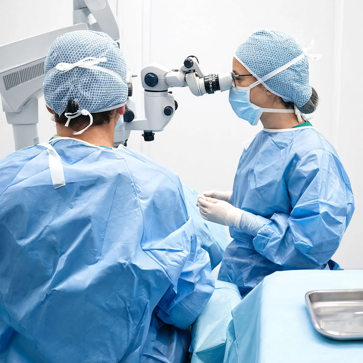 Due chirurghi in sala operatoria durante intervento oculistico, uno al microscopio operatorio e l'altra con strumenti chirurgici sterili