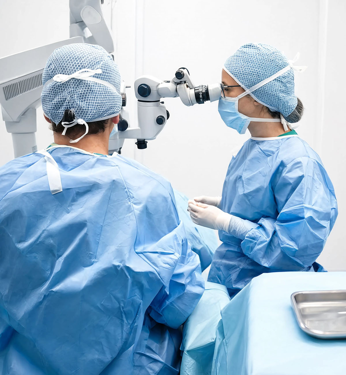 Due chirurghi in sala operatoria durante intervento oculistico, uno al microscopio operatorio e l'altra con strumenti chirurgici sterili