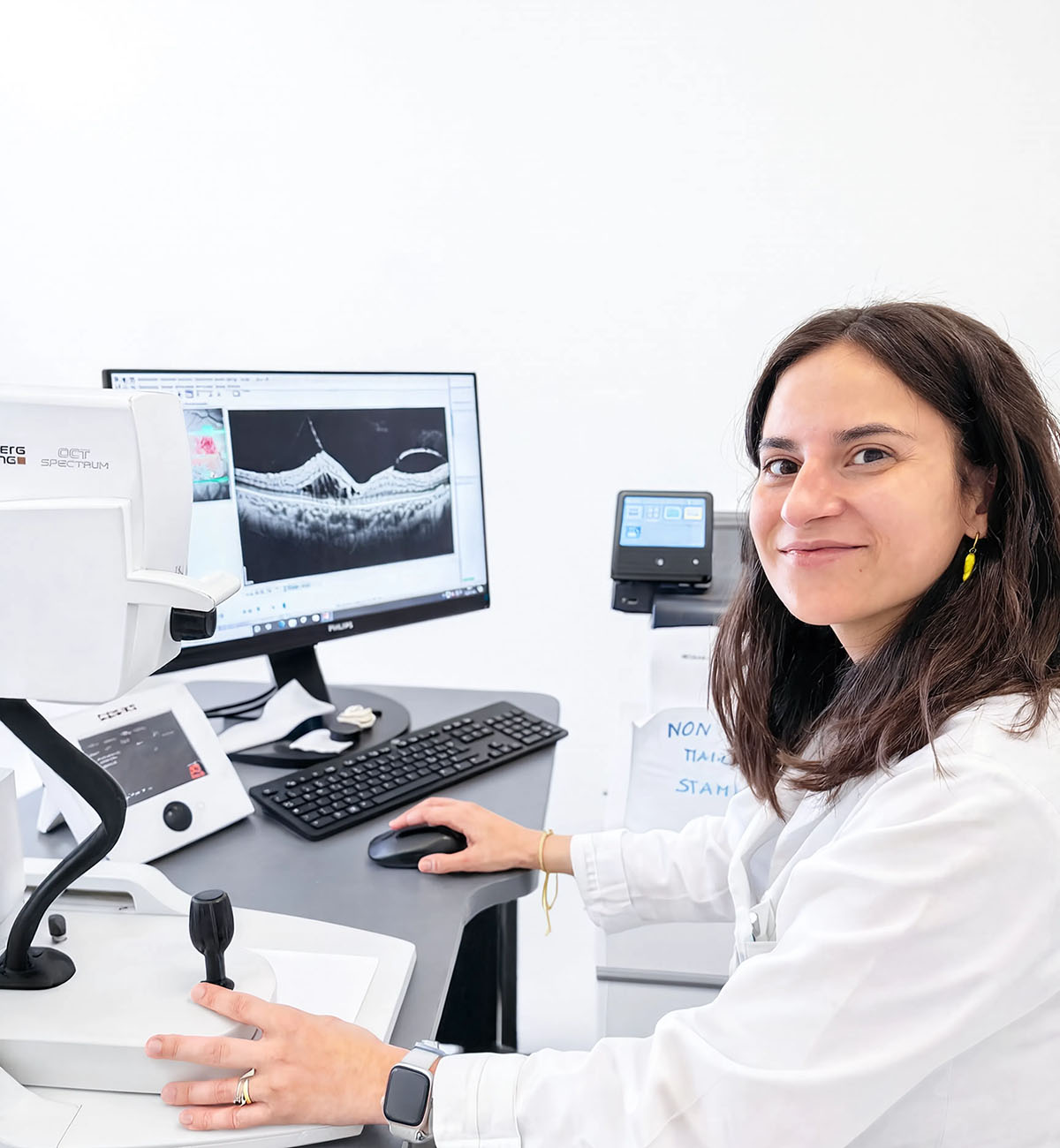Oculista sorridente seduta alla strumentazione OCT durante l'esame della retina, con scansione visibile a monitor