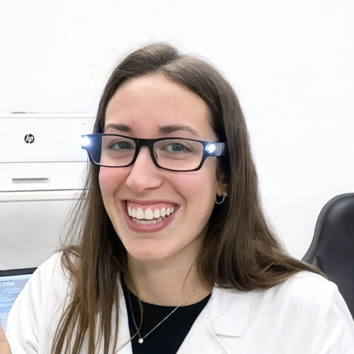 Ritratto di oculista sorridente con occhiali dotati di luci LED integrate, in camice bianco nello studio